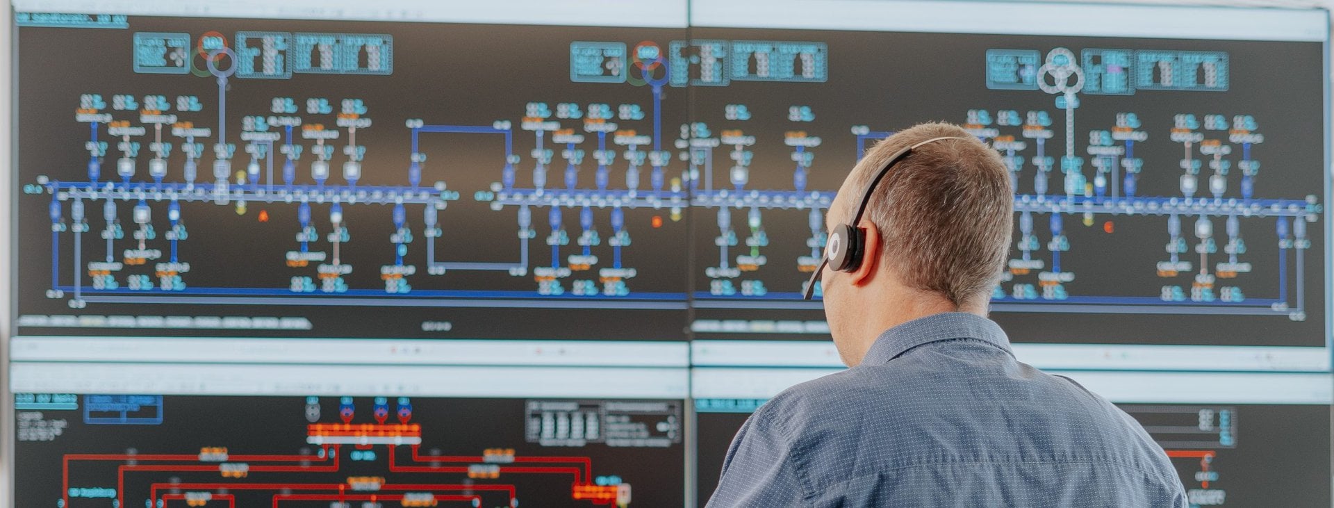 Eine mit dem Rücken zugewandte Person mit Kopfhörer, an einem Arbeitsplatz mit vielen Bildschirmen